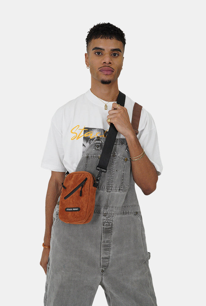 Person wearing gray overalls with a brown Stash bag and white t-shirt on a white background